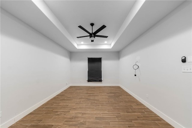 empty room featuring baseboards, recessed lighting, wood finished floors, a raised ceiling, and a ceiling fan