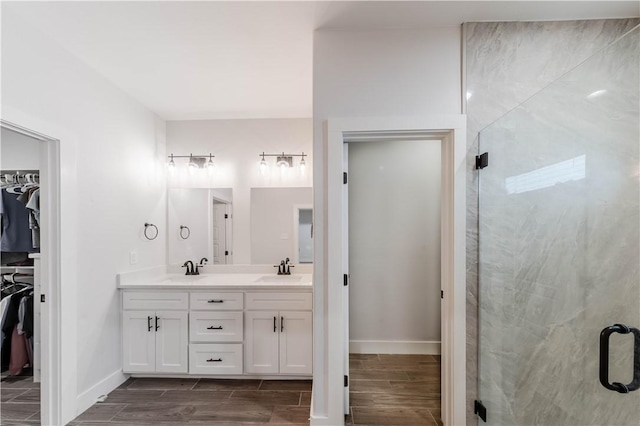 full bath with a walk in closet, wood finish floors, double vanity, a stall shower, and a sink