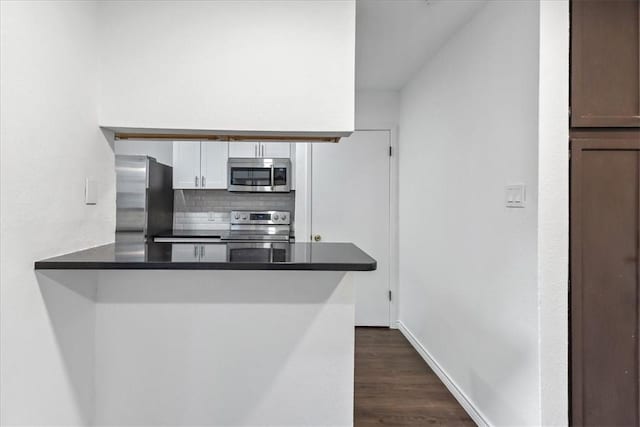 kitchen with dark hardwood / wood-style floors, backsplash, kitchen peninsula, white cabinets, and appliances with stainless steel finishes