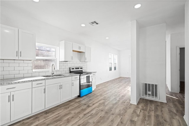 kitchen featuring stainless steel electric stove, white cabinets, light stone countertops, and sink