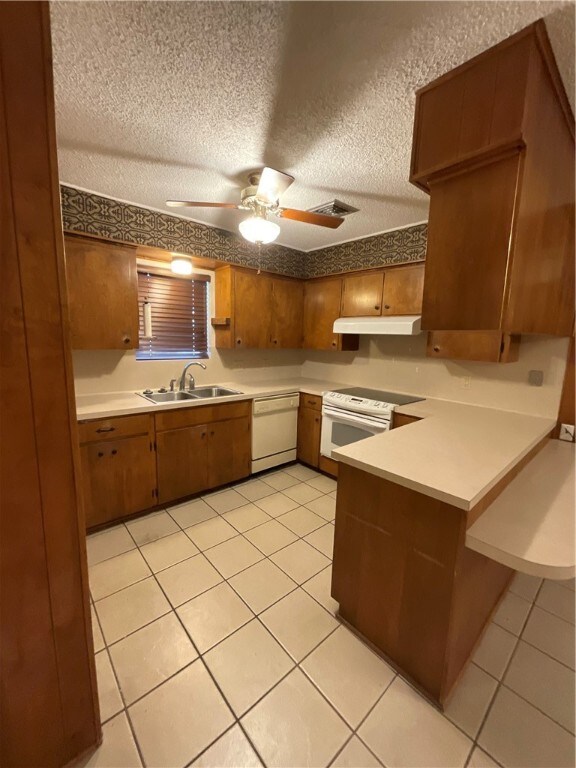 kitchen with a textured ceiling, white appliances, light tile patterned floors, sink, and kitchen peninsula