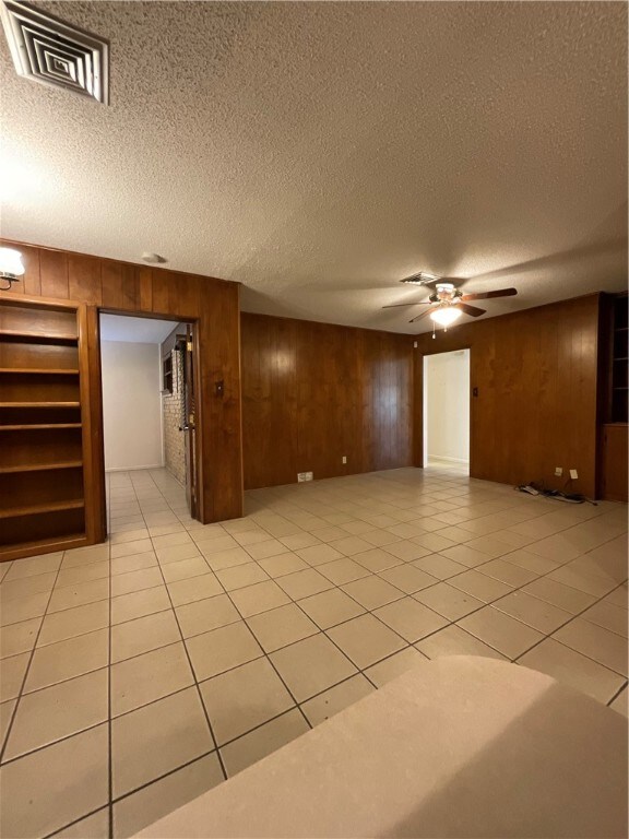 empty room featuring wood walls, light tile patterned flooring, ceiling fan, and a textured ceiling