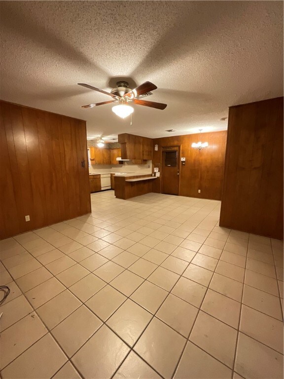 interior space with wood walls, a textured ceiling, ceiling fan, and light tile patterned flooring