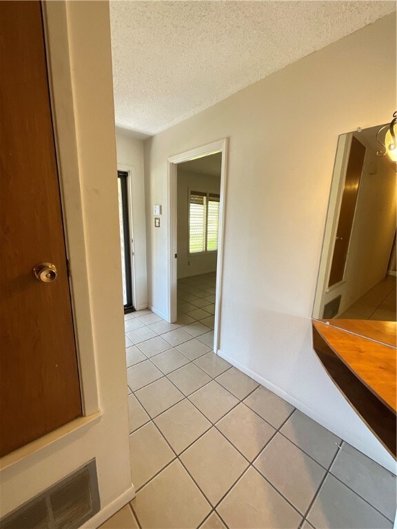 corridor with light tile patterned flooring and a textured ceiling