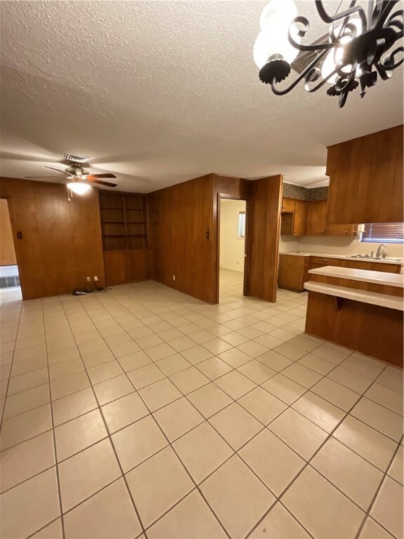 interior space featuring ceiling fan with notable chandelier, wooden walls, a textured ceiling, sink, and light tile patterned floors