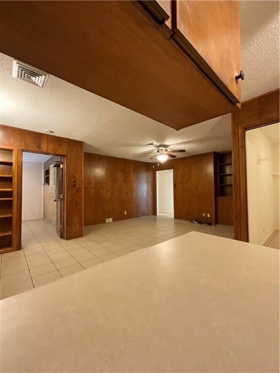 tiled empty room featuring wood walls, ceiling fan, and a textured ceiling