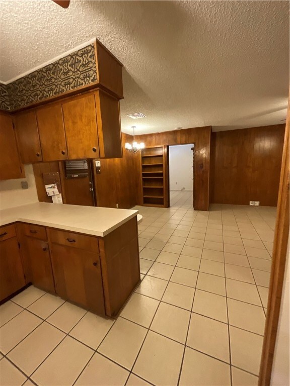 kitchen with wood walls, a textured ceiling, light tile patterned flooring, and ceiling fan with notable chandelier