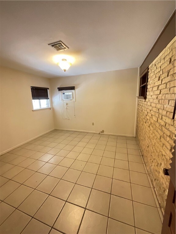 spare room featuring light tile patterned flooring, brick wall, and a wall mounted air conditioner