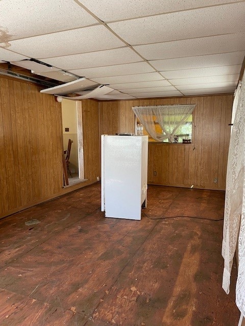 basement featuring dark hardwood / wood-style floors, a drop ceiling, white fridge, and wood walls