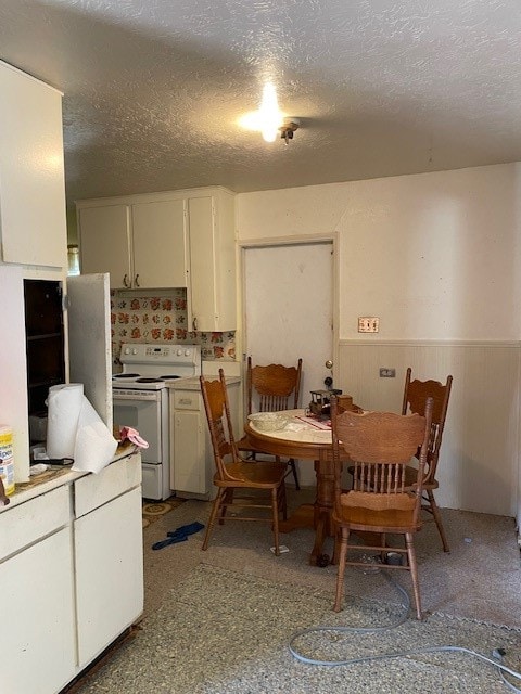 kitchen with a textured ceiling, white electric stove, stainless steel refrigerator, and wooden walls