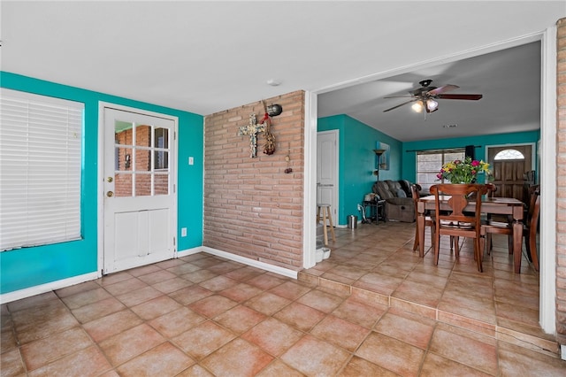 unfurnished dining area with ceiling fan, light tile patterned flooring, and brick wall