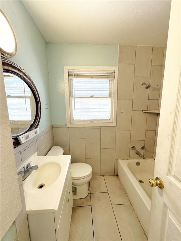 bathroom featuring tile walls, toilet, vanity,  shower combination, and tile patterned flooring