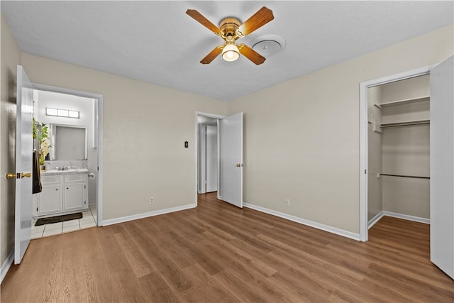 unfurnished bedroom with wood-type flooring, connected bathroom, ceiling fan, a closet, and a walk in closet