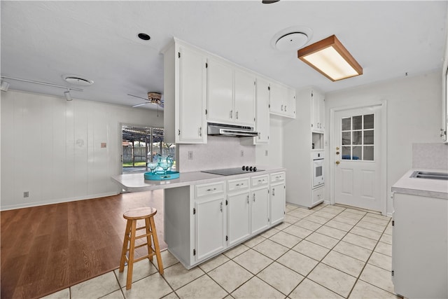 kitchen with white cabinetry, light wood-type flooring, a kitchen breakfast bar, black electric cooktop, and ceiling fan