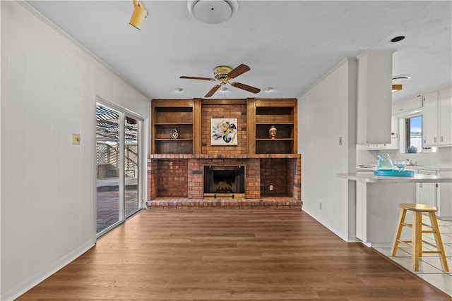 unfurnished living room with built in features, hardwood / wood-style flooring, ceiling fan, and a brick fireplace