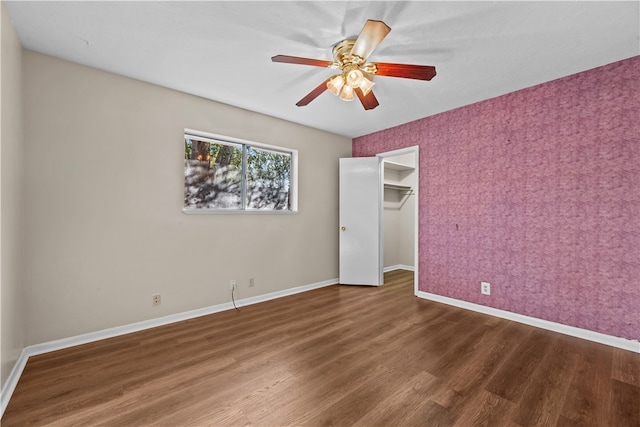 unfurnished bedroom featuring dark wood-type flooring, ceiling fan, a closet, and a walk in closet