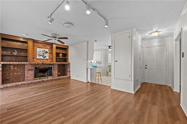 unfurnished living room with a fireplace, rail lighting, light hardwood / wood-style flooring, and built in shelves