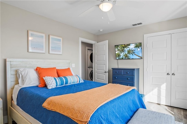 bedroom featuring ceiling fan, stacked washer / dryer, wood finished floors, visible vents, and a closet