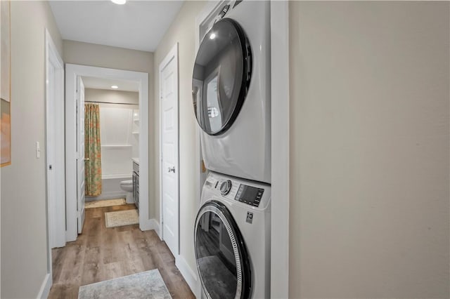 laundry area with baseboards, laundry area, stacked washer and clothes dryer, and light wood-style floors