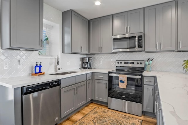 kitchen with light stone counters, light wood finished floors, stainless steel appliances, gray cabinets, and a sink