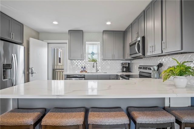 kitchen featuring light stone counters, a peninsula, a sink, appliances with stainless steel finishes, and gray cabinets