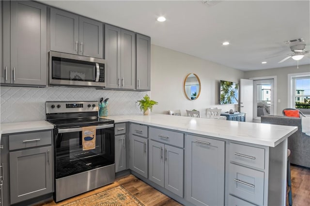 kitchen featuring dark wood finished floors, gray cabinetry, appliances with stainless steel finishes, open floor plan, and a peninsula