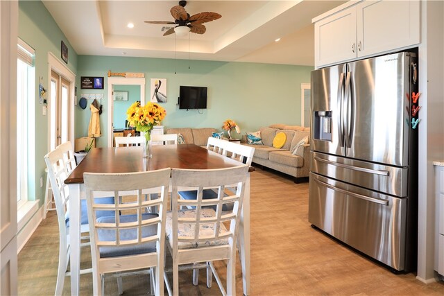 dining space with light wood-type flooring, a healthy amount of sunlight, ceiling fan, and a raised ceiling