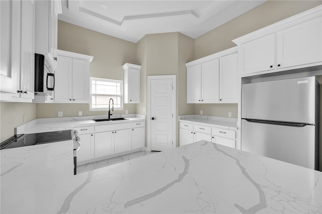 kitchen featuring sink, stainless steel appliances, light stone counters, a tray ceiling, and white cabinets