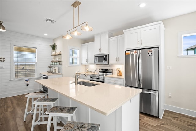 kitchen with stainless steel appliances, sink, decorative light fixtures, white cabinets, and an island with sink