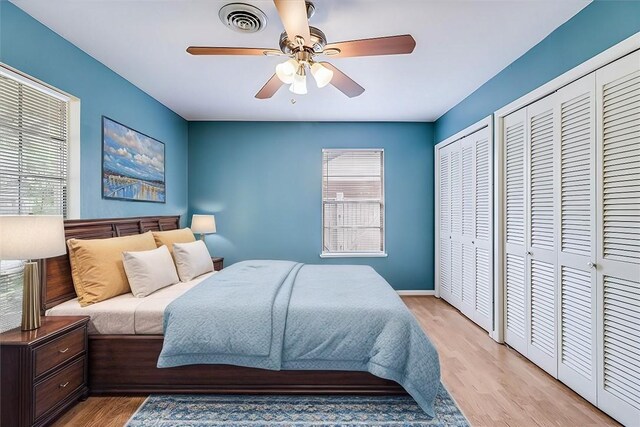 bedroom featuring two closets, light hardwood / wood-style flooring, multiple windows, and ceiling fan