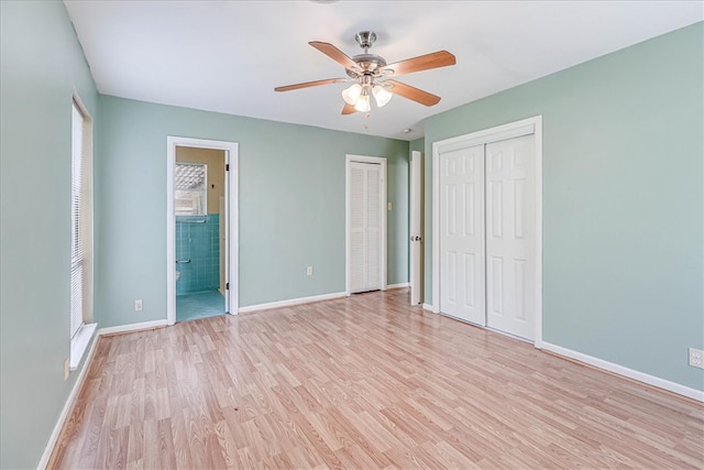 unfurnished bedroom with connected bathroom, light hardwood / wood-style floors, ceiling fan, and multiple closets