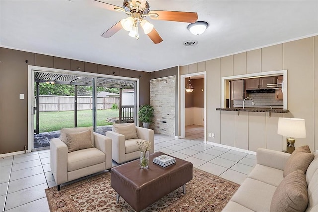 living room featuring ceiling fan, light tile patterned floors, sink, and ornamental molding