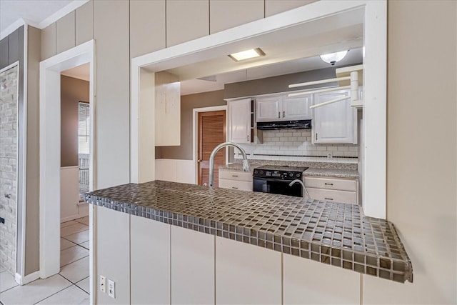 kitchen with decorative backsplash, black range with electric cooktop, light tile patterned floors, tile countertops, and white cabinetry