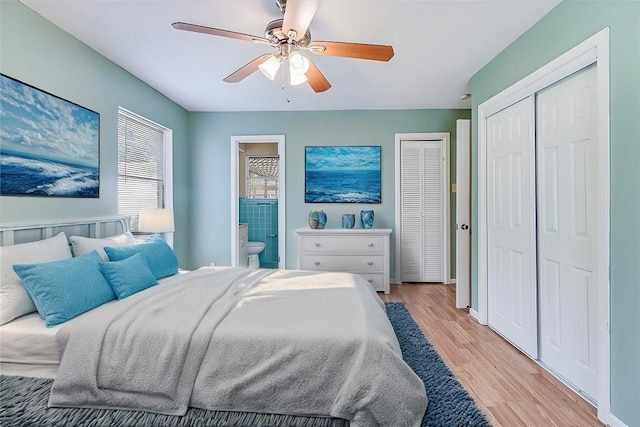 bedroom featuring light wood-type flooring, ensuite bathroom, ceiling fan, and multiple closets