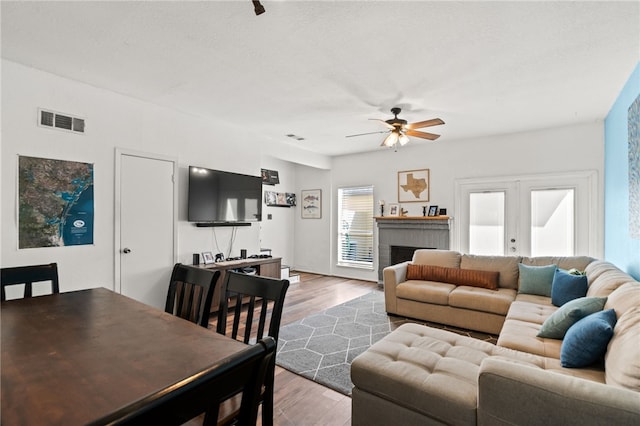 living room featuring ceiling fan, a brick fireplace, wood finished floors, and visible vents