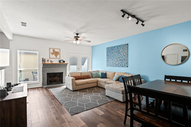 living room featuring dark wood-style floors, visible vents, a ceiling fan, a fireplace, and rail lighting