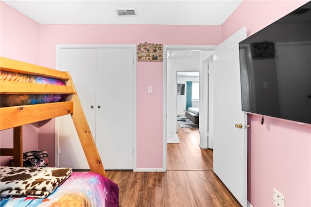 bedroom with wood finished floors, visible vents, and a closet