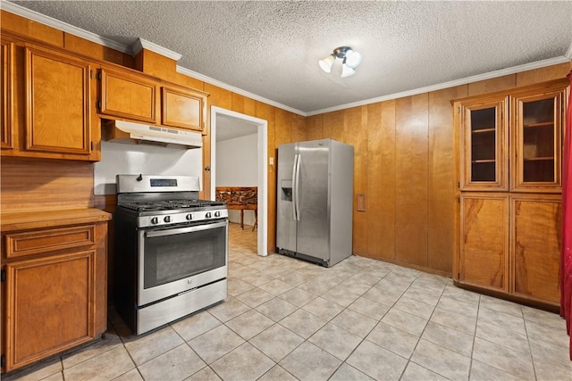 kitchen with wooden walls, light tile patterned floors, a textured ceiling, ornamental molding, and stainless steel appliances