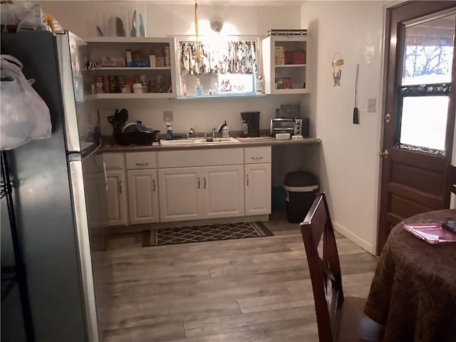 kitchen featuring sink, white cabinetry, stainless steel refrigerator, and light hardwood / wood-style floors