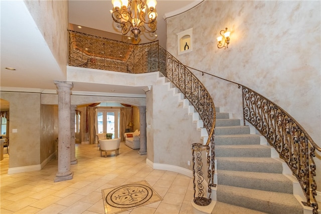 stairway with a high ceiling, ornamental molding, a chandelier, ornate columns, and french doors