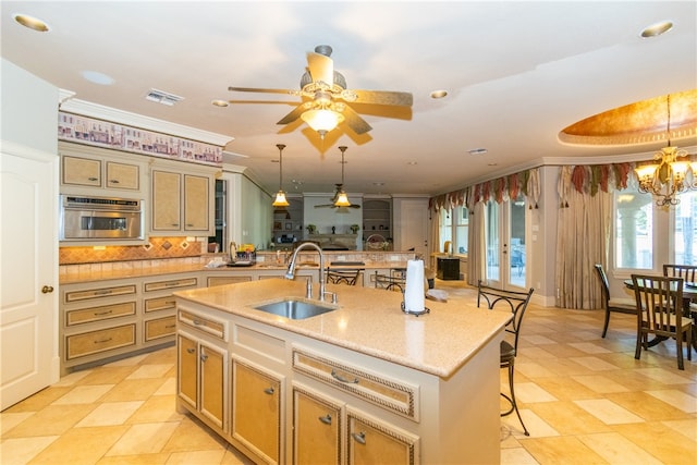 kitchen featuring crown molding, a kitchen bar, hanging light fixtures, sink, and a kitchen island with sink