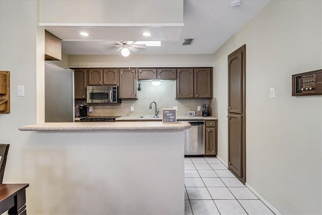 kitchen with appliances with stainless steel finishes, kitchen peninsula, light tile patterned floors, ceiling fan, and sink