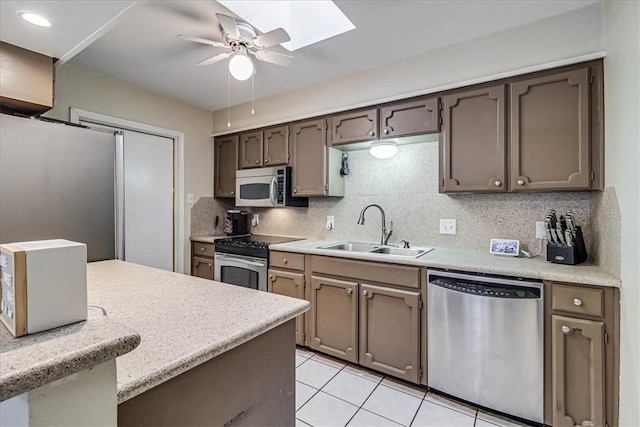 kitchen featuring sink, light tile patterned floors, a skylight, backsplash, and appliances with stainless steel finishes