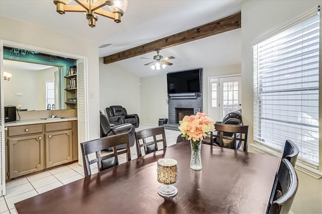 dining room featuring sink, light tile patterned flooring, ceiling fan with notable chandelier, a brick fireplace, and beam ceiling