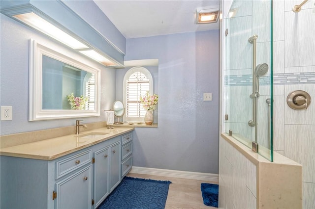 full bathroom with wood finished floors, a tile shower, vanity, and baseboards