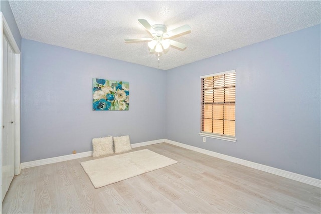 empty room with a ceiling fan, light wood-style flooring, baseboards, and a textured ceiling