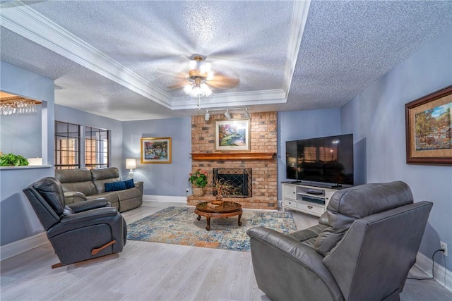 living room featuring a tray ceiling, ornamental molding, a brick fireplace, a textured ceiling, and baseboards