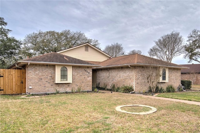 ranch-style house with brick siding, fence, a front lawn, and roof with shingles