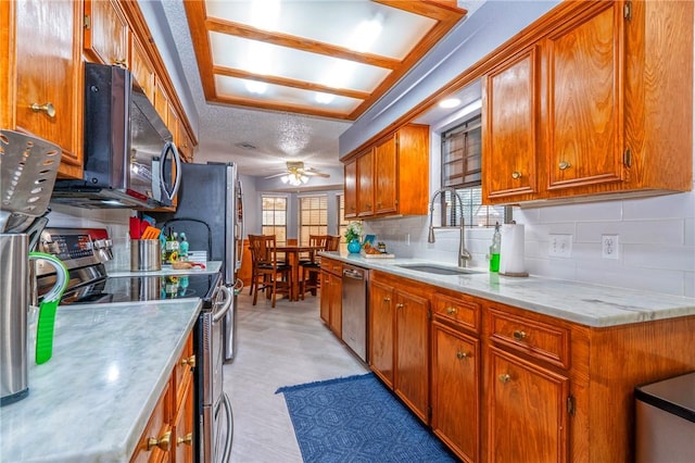 kitchen featuring tasteful backsplash, brown cabinetry, appliances with stainless steel finishes, light countertops, and a sink