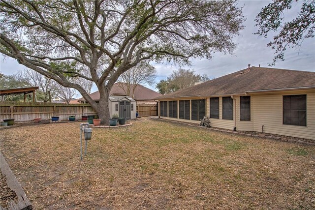 view of yard featuring a storage unit, an outdoor structure, a fenced backyard, and a sunroom